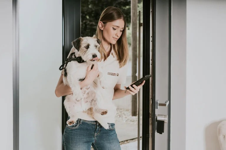 Femeie cu caine in brate care descuie incuietoarea Nuki Smart Lock Pro de pe telefon Femeie cu caine in brate care descuie incuietoarea Nuki Smart Lock Pro de pe telefon